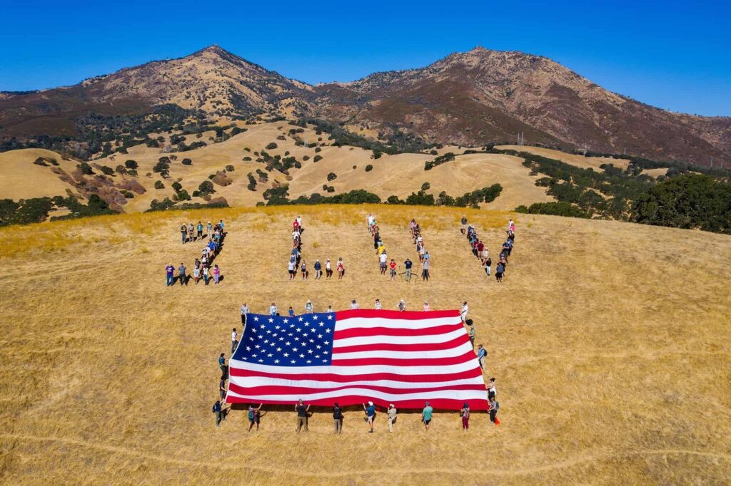 People lined up as a human banner to spell 1 LUV with American flag in front and Mount Diablo in the background