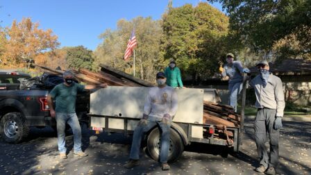 People posing for a photo in front of a truck bed filled with collected debris