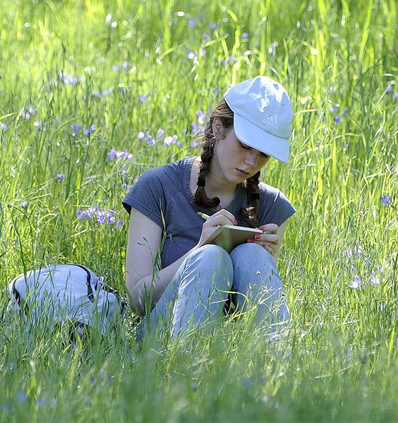 a young woman journaling amid wildflowers during a Conservation Collaboration Agreement