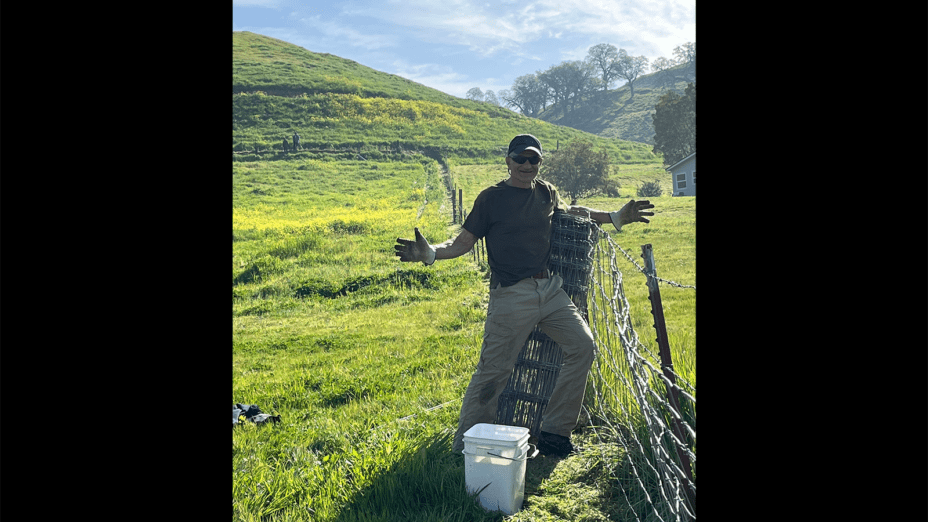 Man posing with arms out while leaning against a fence