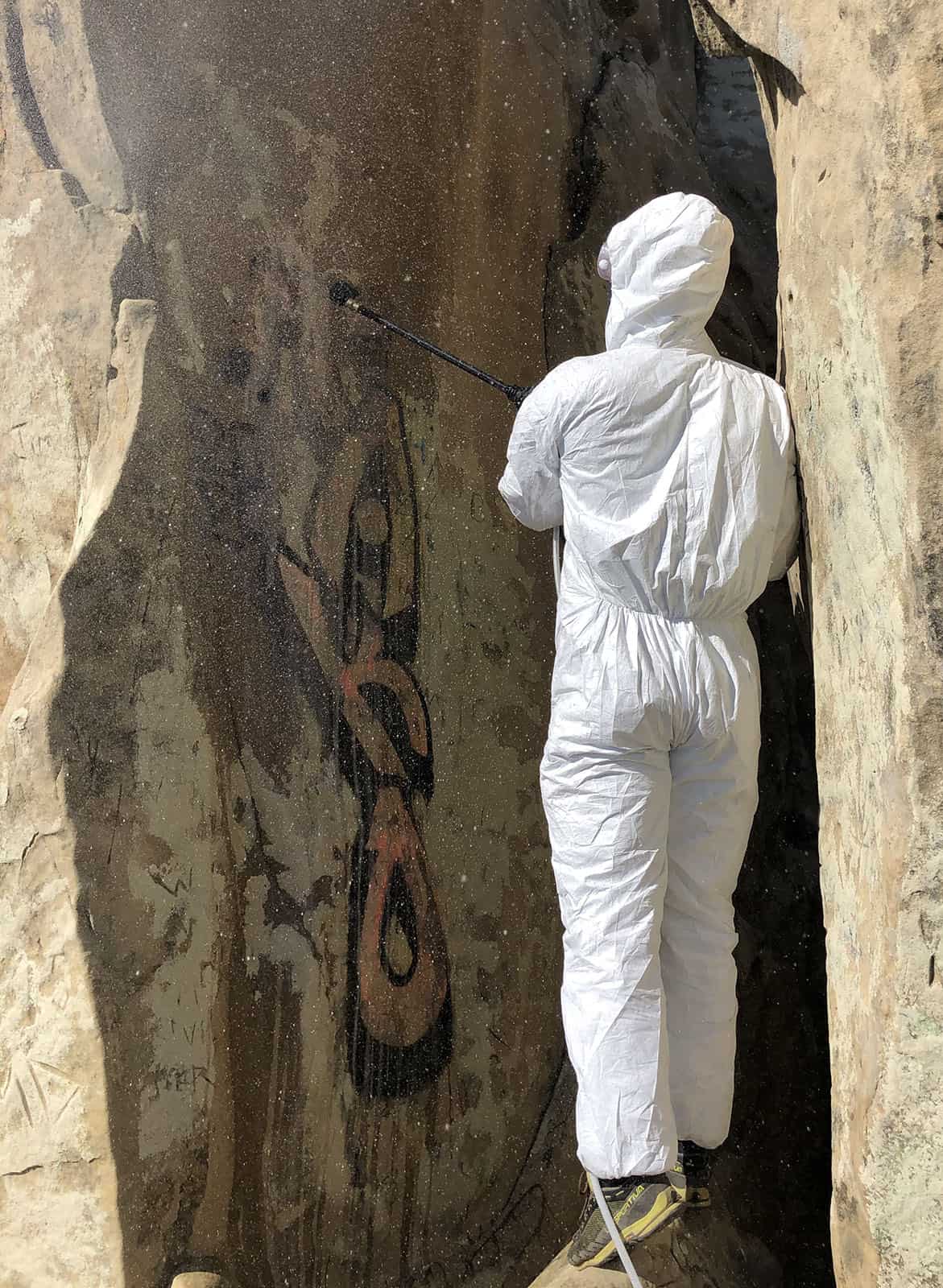 Person in haz mat suit removing graffiti from Castle Rocks in Pine Canyon