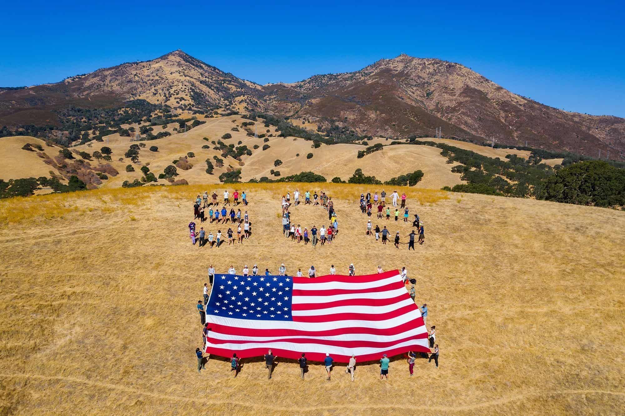 Aerial view of people lined up to spell SOS with American flag in front and Mount Diablo in the background