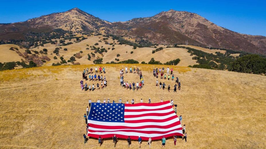 Aerial view of people lined up to spell SOS with American flag in front and Mount Diablo in the background