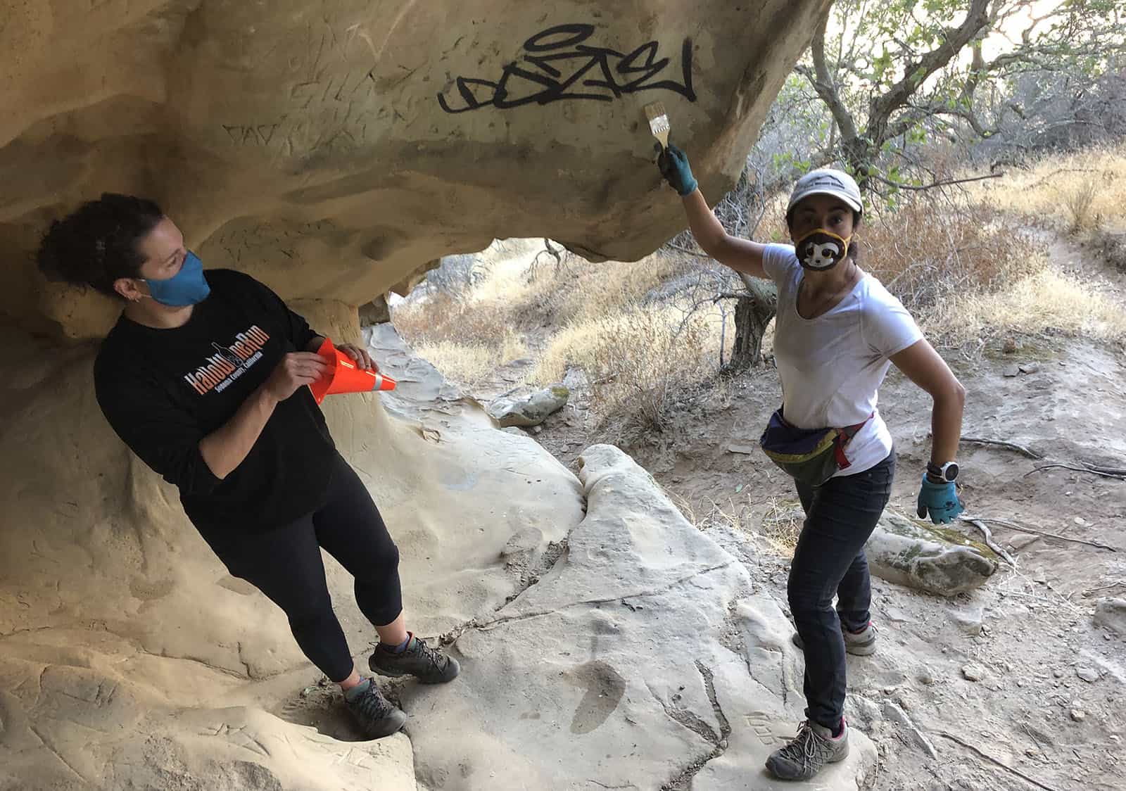 Two women removing graffiti from Castle Rocks