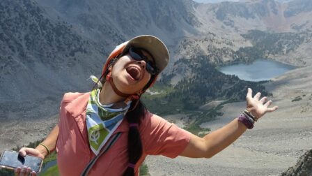 smiling woman standing in front of some mountains and a lake