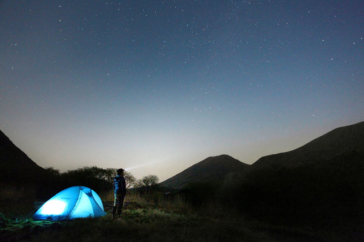 a person looking at the night sky next to their well lit tent