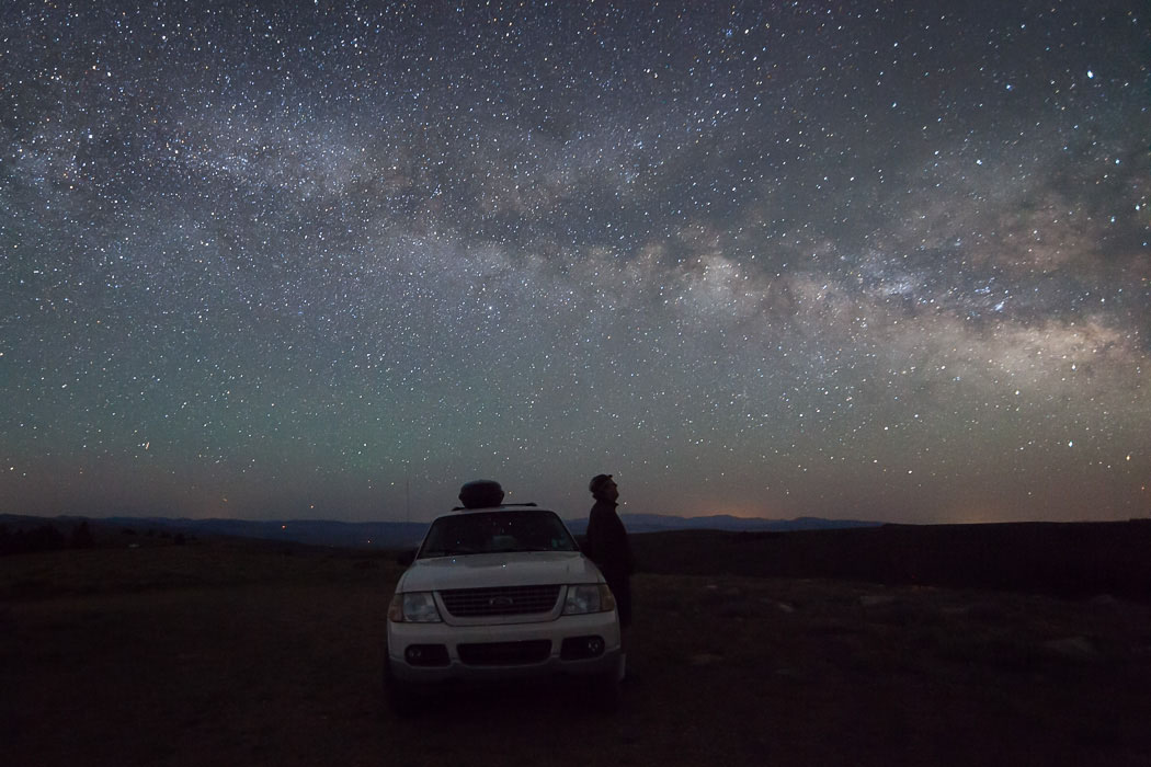 Person standing next to a car and looking at the stars