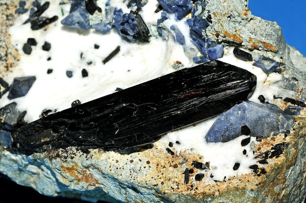 Benitoite is often found with a whole host of other rare minerals and gems like the prominent Neptunite crystal in this photo as well as Joaquinite and Natrolite.