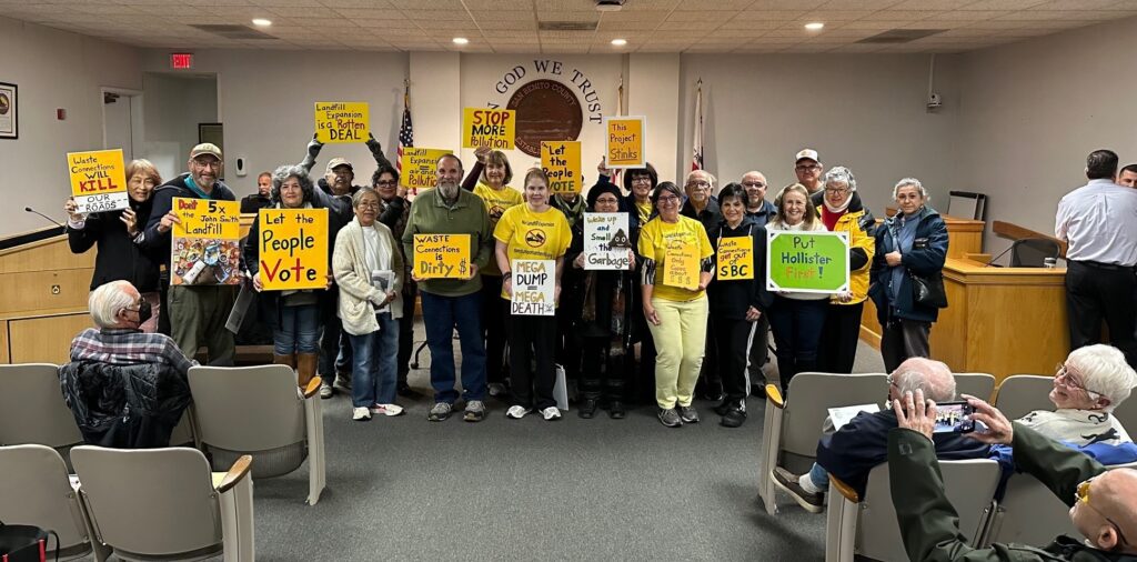 a group of people in the city council hall hold various signs protesting the landfill